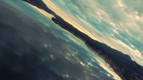 Smooth rotating aerial over clear lake water reflecting bright sky Stockbeeldmateriaal 328898475