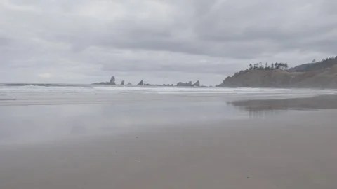 Smooth sandy beach at low tide with cliffs and seastacks in background Video stock 332255365