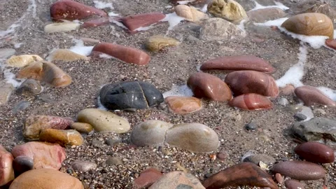 Smooth stones on sandy shore gently washed by small foamy waves Stock Footage 321476444