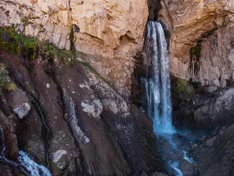 A smooth stream of water flows down from a cave in the high rocks of the Cauc Stock Photos