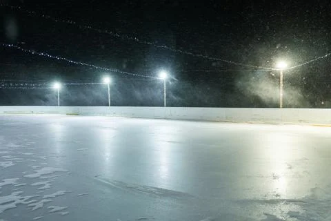 Smooth surface of an empty outdoor ice rink reflecting bright floodlights under Stock Photos