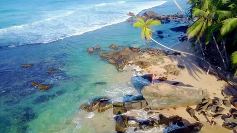 Smooth waves wash rocks on sandy beach with tourist Stock Footage 248756310