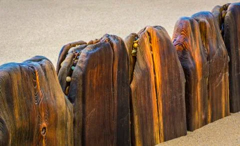 Smooth wooden structures in a row creating a barrier in the sand with coloured p Stock Photos