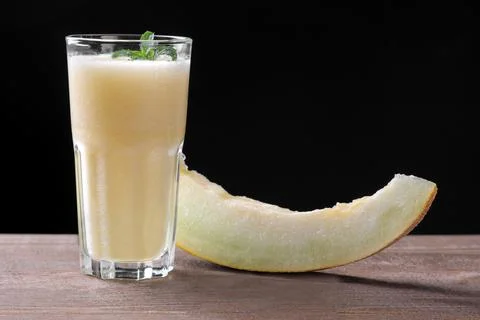 Smoothies of melon next to a slice of melon on a brown wooden table on a blac Stock Photos