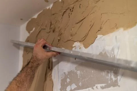 Smoothing beige plaster on wall surface using trowel in home renovation project Stock Photos