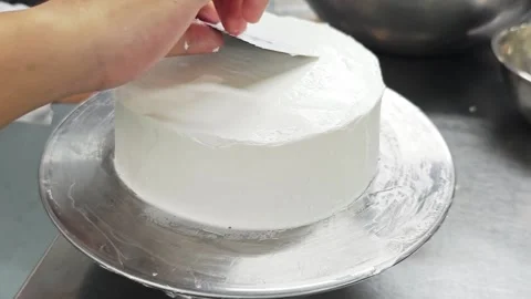 Smoothing a white cream cake with a plastic scraper. 動画素材 344745003