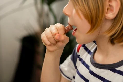 Snack time joy: A young boy, 10, munches on a sausage, embracing the delici.. Stock Photos