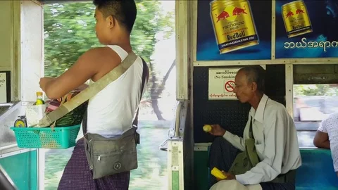Snack vendor stands inside circular train, local man eats corn, Yangon, Myanmar Видео 78278092