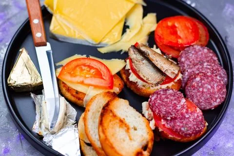 Snacks on a plate with cheese, tomatoes, bread, salami, and sardines, ready for Stock Photos