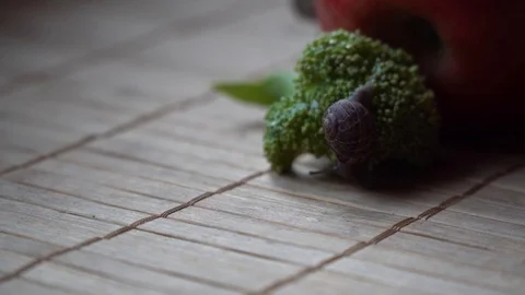 Snail crawls over the red apple and green broccoli, cute animal, film background Stock Footage 89579403