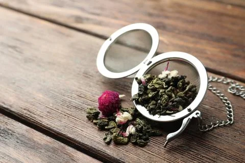 Snap infuser with dried herbal tea leaves and flowers on wooden table, closeu Stock Photos