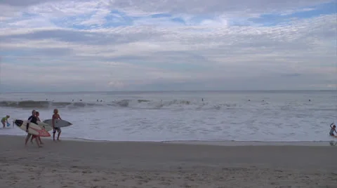 Snap zoom to overcast beach, with surfers walking Stock Footage 24453191