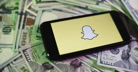 Snapchat Logo on iphone surrounded by $100 Bills. Snapchat Profits Layout Stock Footage 169006373