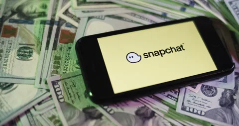 Snapchat Logo on iphone surrounded by $100 Bills. Snapchat Profits Layout Stock Footage 169006384