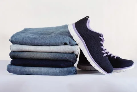 Sneakers and a stack of jeans on a white background Stock Photos