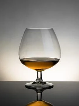Snifter of brandy in elegant typical cognac glass on white light on grey back Stock Photos