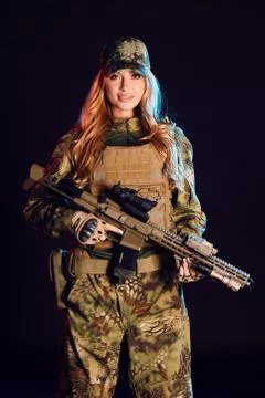 Sniper woman in ghillie suit, cap, plate carrier holds airsoft rifle in studio Stock Photos