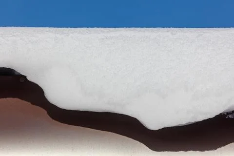 Snow blankets a dark, curved surface beneath a clear blue sky Stock Photos