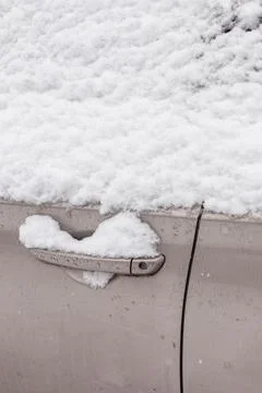 Snow blankets the surface of a car with a handle partially visible. The scene Photos