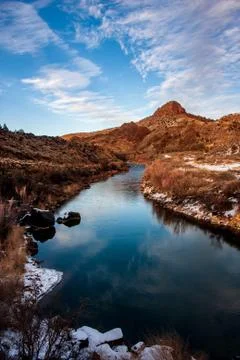 Snow bordering quiet stream looking north toward mountains Stock Photos