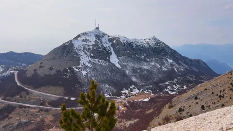 Snow capped mountain peak with communication tower and winding road Видео 342492155