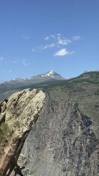 Snow-capped mountain peak with forested slopes, rocky outcrops, and clear blue s Stock Photos