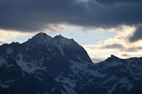 Snow-Capped Mountain Peak under Dramatic Sunset Clouds 写真素材