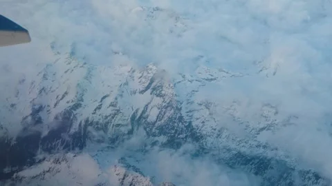 Snow capped mountain peaks pierce through drifting clouds rugged alpine terrain Видео 343673551