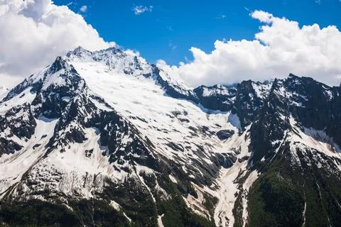 Snow-capped mountain peaks under a bright blue sky with scattered clouds Stock Photos