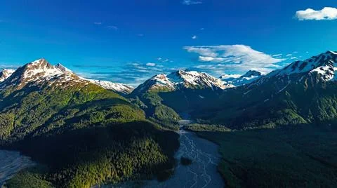 Snow-capped mountain range with green forest and river Stock Photos