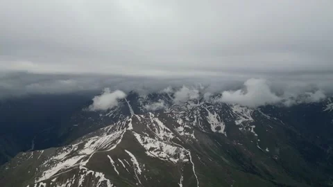 Snow-capped mountain range under cloudy sky with gradual fog coverage Stock Footage 336963502