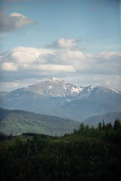 Snow-capped mountain range under a blue sky with fluffy clouds and lush green Stock Photos