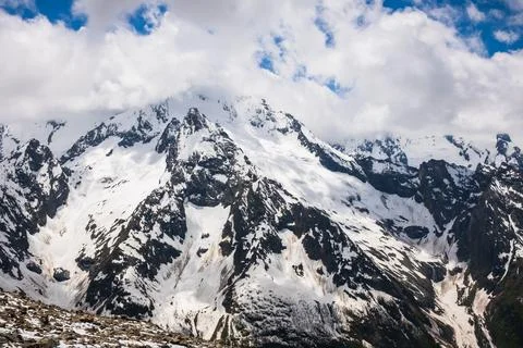 Snow-capped mountain range under a cloudy sky with rocky terrain and patches of Stock Photos