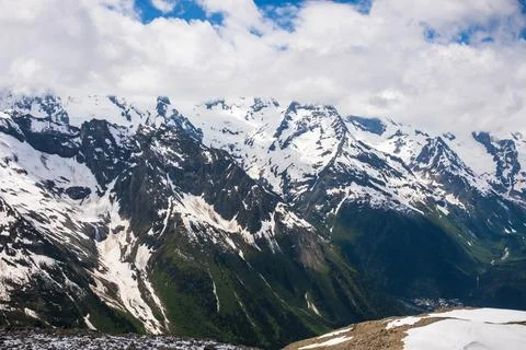 Snow-capped mountain range under a cloudy sky with green valleys and rocky Stock Photos
