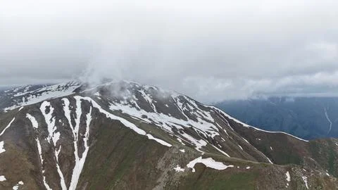 Snow-capped mountain range under cloudy sky with green slopes visible Stock Photos