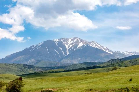 Snow-capped mountain rises above green rolling hills Stock Photos