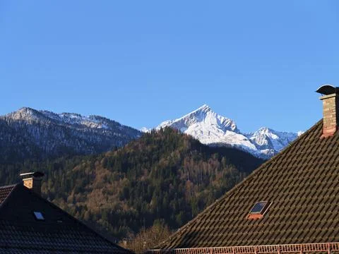 Snow-capped mountain rises over rooftops on a clear day in a tranquil village Stock Photos