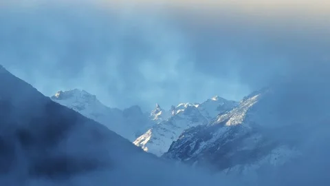 Snow capped mountain shrouded in clouds and mist Stockbeeldmateriaal 303982111