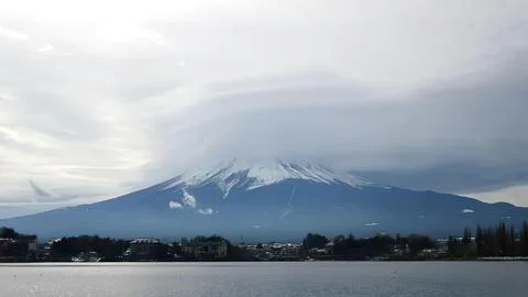 Snow-capped mountain view over city and lake on cloudy day Stock Photos