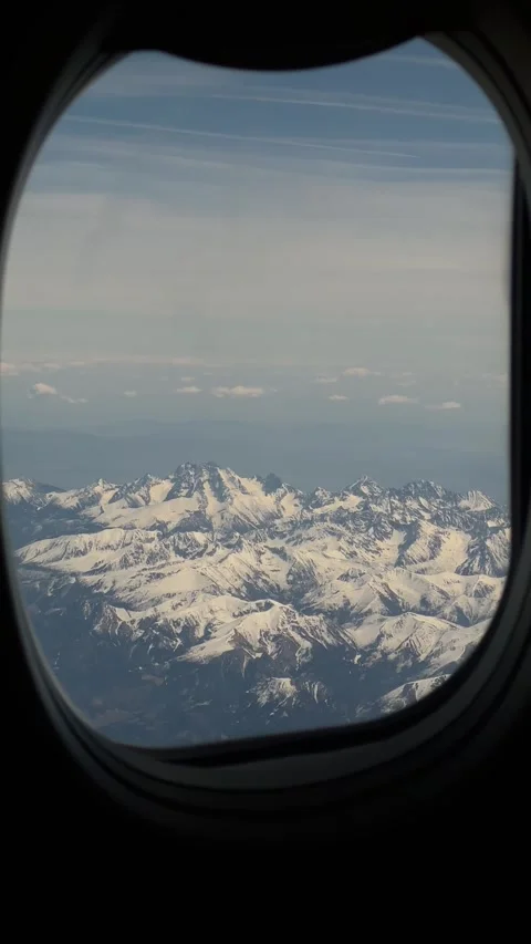 Snow-capped mountains and clouds seen through airplane window during flight Stock Footage 346559791