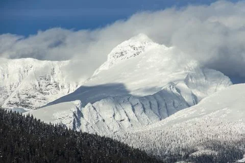 Snow-capped mountains hover under dramatic clouds in a peaceful winter land.. Stock Photos