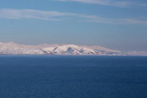 Snow capped mountains on lake sevan in clear weather at sunset Stock Photos