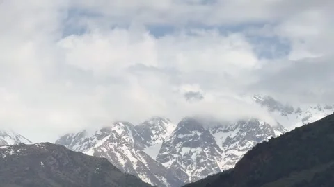 Snow-capped mountains partially covered in clouds, lush dark green hills in Vídeos de archivo 276424147