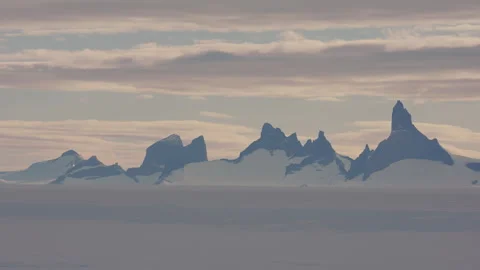 Snow-capped mountains rise under soft clouds in Antarctica Stock Footage 288191497