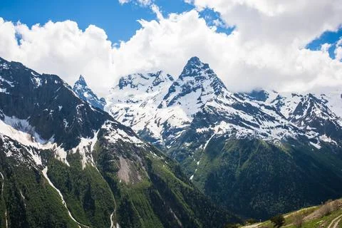 Snow-capped mountains under a blue sky with fluffy clouds, showcasing rugged 写真素材