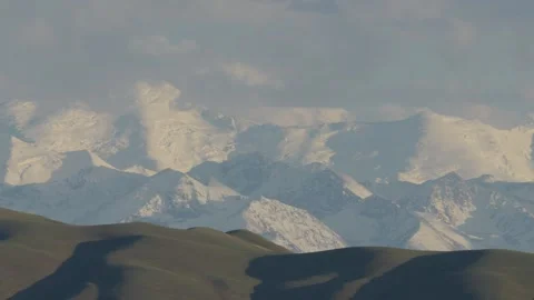 Snow-capped mountains under clouds at sunset light, Kazakhstan Видео 333910642