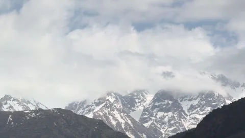 Snow-capped mountains under a cloudy sky, showcasing a serene and majestic Stock Footage 276423991