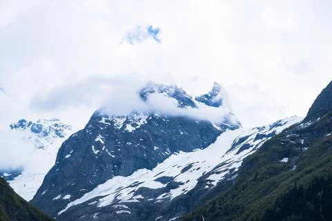 Snow-capped mountains under cloudy sky with lush green slopes and rocky terrain Stock Photos
