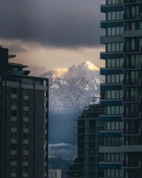 Snow-capped mountains viewed between buildings Stock Photos