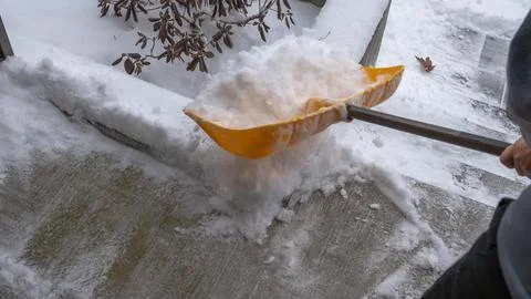 Snow cleaning service worker using a yellow shovel to clear snow from a concrete Stock Photos